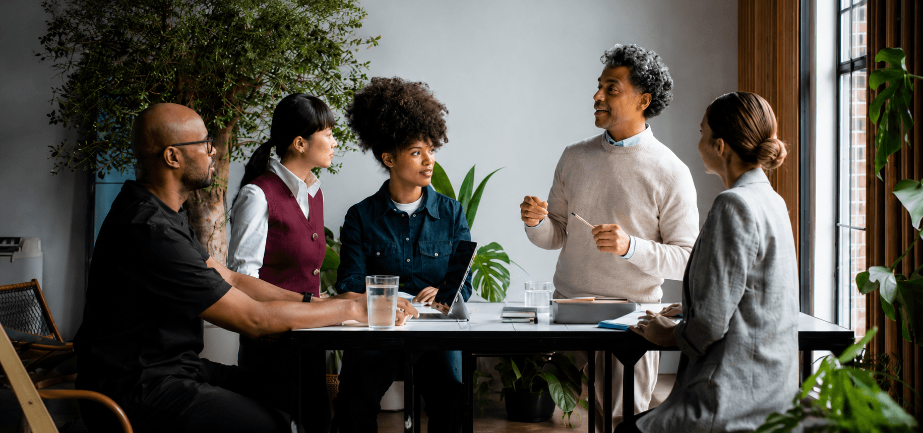 Five colleagues in a strategy meeting around a table in a plant-filled office